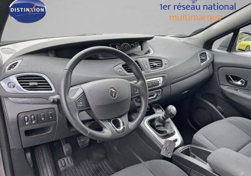 Vue intérieure côté conducteur du Renault Scénic III gris de 2015, montrant le volant, tableau de bord et levier de vitesse manuel.