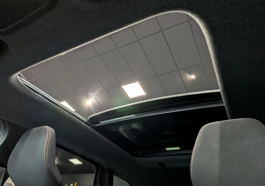 Toit ouvrant panoramique ouvert vu de l'intérieur sur les sièges avant du Dacia Bigster Hybrid-G 150 4x4 gris schiste.