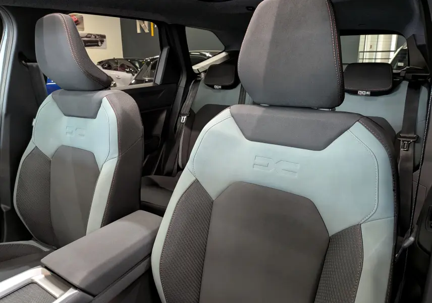 Vue intérieure rapprochée des sièges avant gris clair et noir du Dacia Bigster Hybrid-G 150 4x4, avec surpiqûres orange.