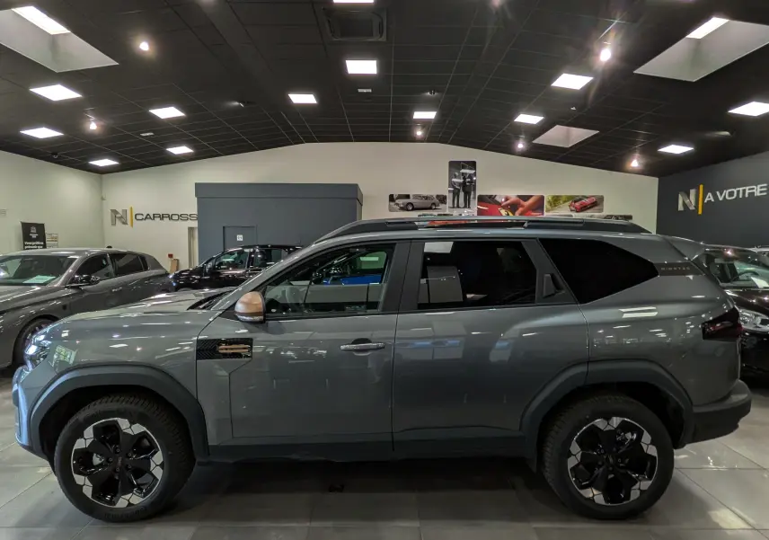 Vue de profil côté gauche du Dacia Bigster Hybrid-G 150 4x4 gris schiste avec jantes bi-ton et rétroviseurs bronze.