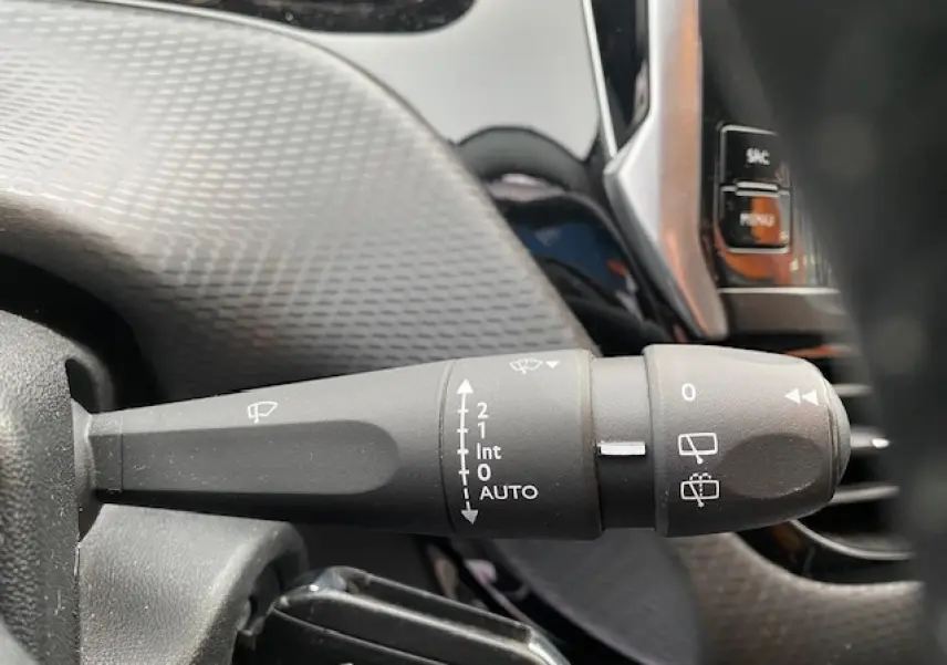 Gros plan sur la commande d'essuie-glace à gauche du volant dans l'habitacle d'un Peugeot 2008 blanc de 2018.