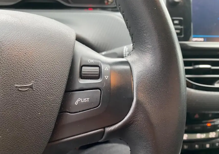 Gros plan sur le volant noir du Peugeot 2008 2018 avec commandes intégrées et écran tactile en arrière-plan.