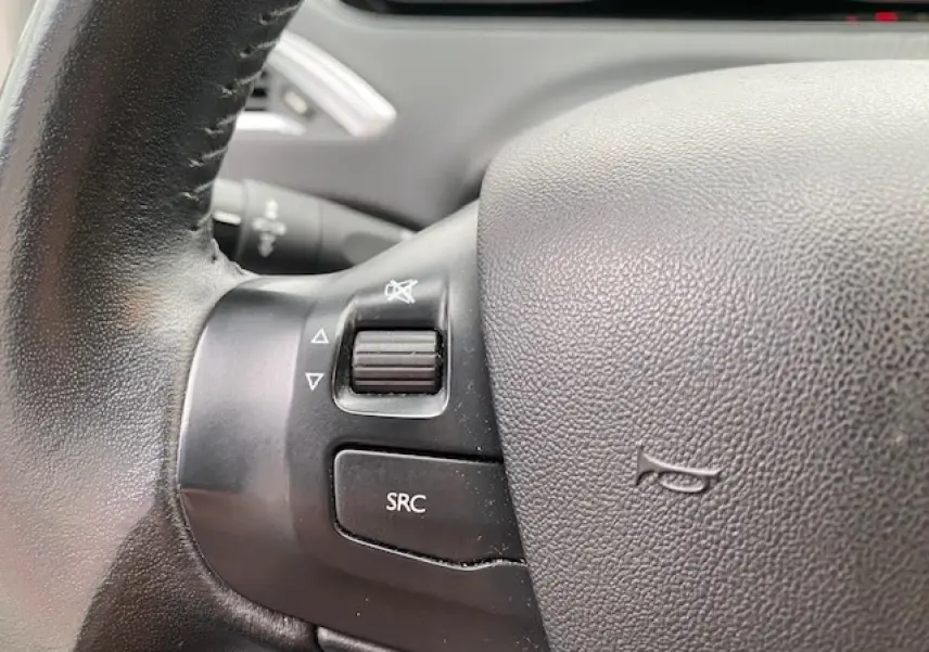 Gros plan sur les commandes audio au volant noir du Peugeot 2008 blanc, version Style Phase 2 de 2018.