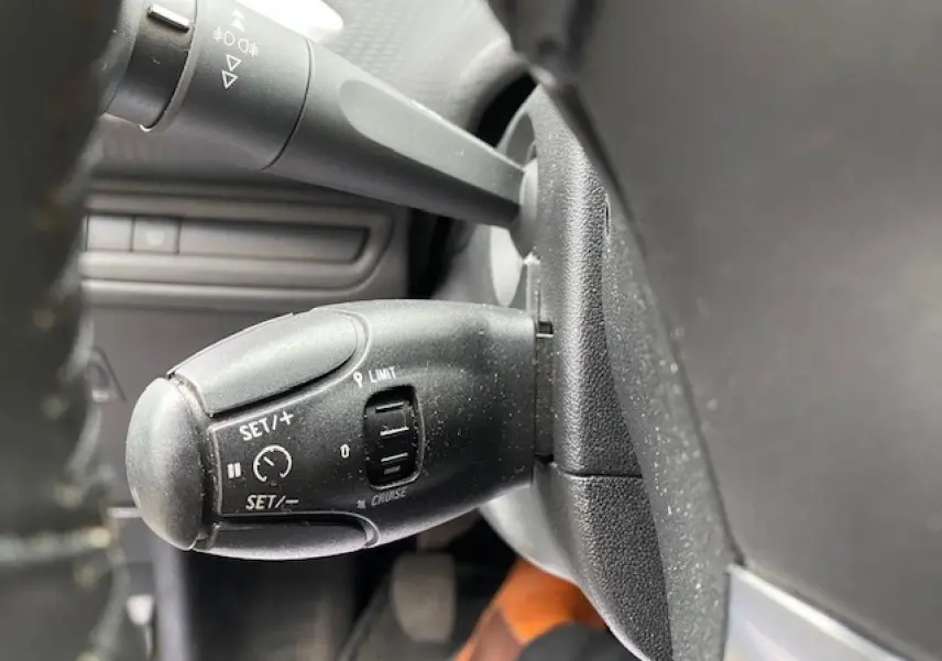 Gros plan sur la commande de régulateur de vitesse à gauche du volant d'un Peugeot 2008 blanc de 2018.
