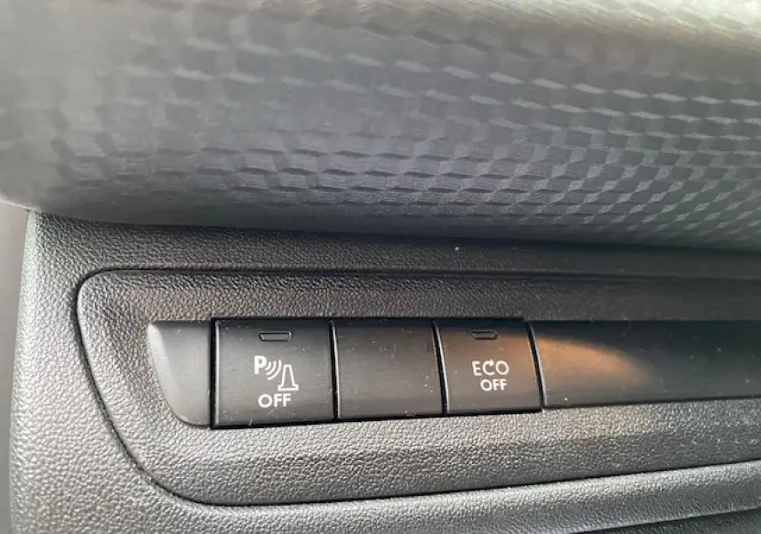 Gros plan sur les boutons de commande du système d'aide au stationnement et mode ECO de la Peugeot 2008 blanche.