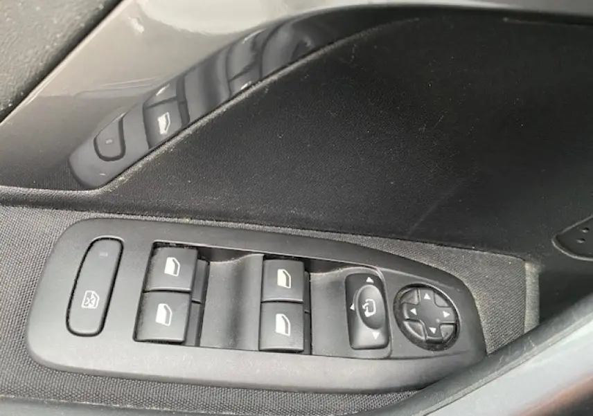 Gros plan sur les commandes des vitres et rétroviseurs côté gauche intérieur d'une Peugeot 2008 blanche de 2018.