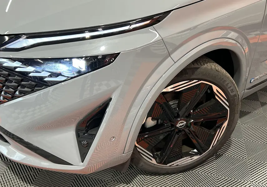 Gros plan sur l'avant droit du Nissan Qashqai gris céramique avec jante noire et blanche et phare LED allumé.