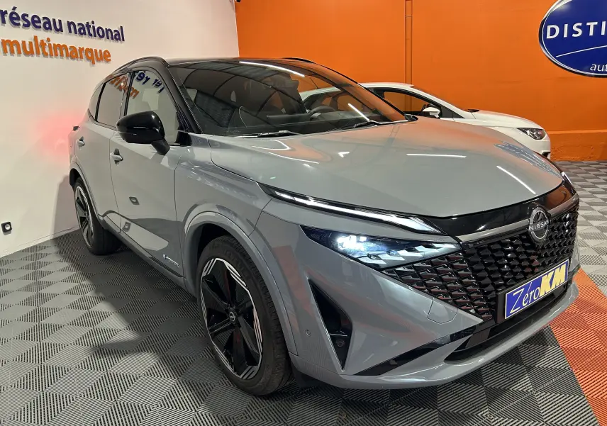 Nissan Qashqai gris céramique avec toit noir, vue 3/4 avant droit, phares LED allumés et calandre noire texturée.
