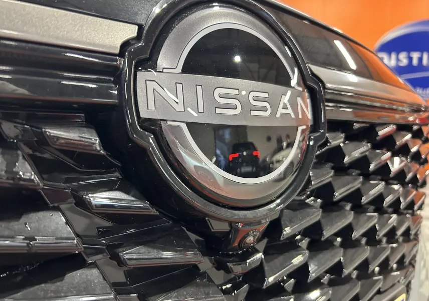 Gros plan sur la calandre noire brillante du Nissan Qashqai 2025 avec logo central et caméra frontale intégrée.