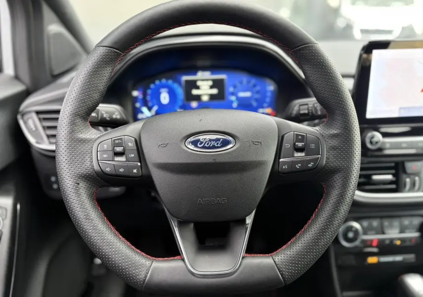 Vue rapprochée du volant ST-Line noir avec surpiqûres rouges du Ford Puma 2023, tableau de bord numérique et écran tactile visibles.