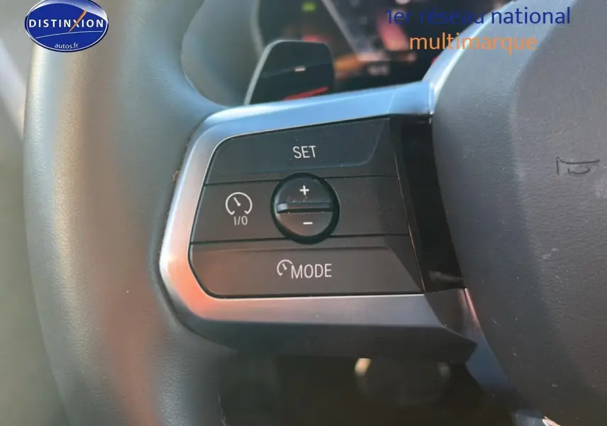 Gros plan sur les commandes du volant à gauche de la BMW Série 1 blanche, boutons de régulateur de vitesse et mode.