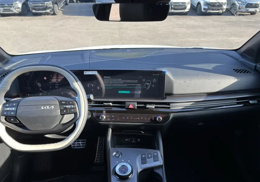 Vue intérieure frontale du tableau de bord du Kia Sportage blanc nacré, avec écran tactile large et volant multifonctions.