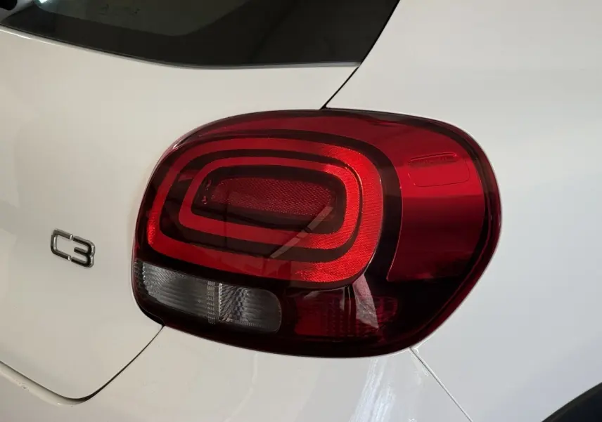 Gros plan sur le feu arrière droit rouge et blanc d'une Citroën C3 blanche, avec logo C3 visible sur la carrosserie.