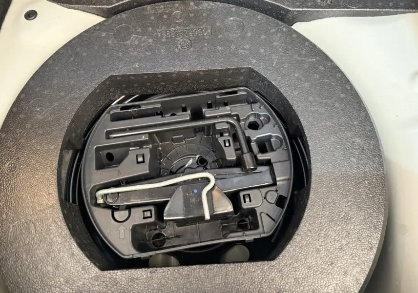 Vue rapprochée de l'espace de rangement sous plancher dans le coffre d'une Citroën C3 blanche, montrant les outils de secours.