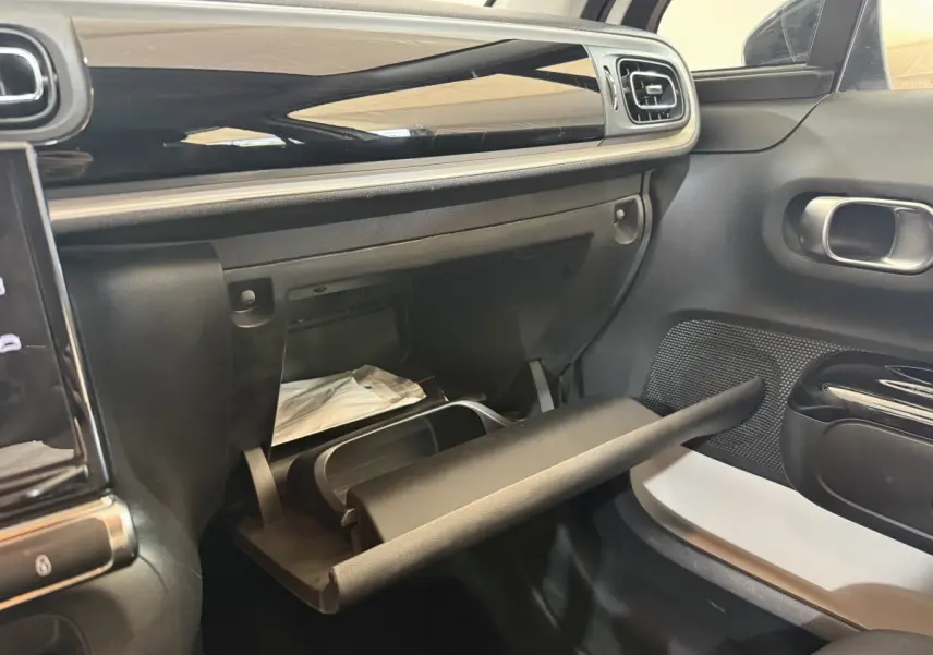 Vue intérieure côté passager de la Citroën C3 blanche 2021 avec boîte à gants ouverte et tableau de bord noir brillant.