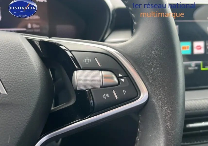 Gros plan sur les commandes gauche du volant cuir multifonction d'une Skoda Fabia bleue, avec écran tactile en arrière-plan.