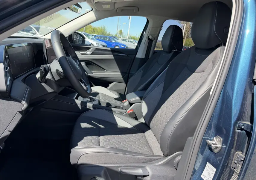 Vue intérieure côté conducteur du Volkswagen Tiguan bleu 2025, sièges avant gris avec motifs géométriques et volant multifonction.