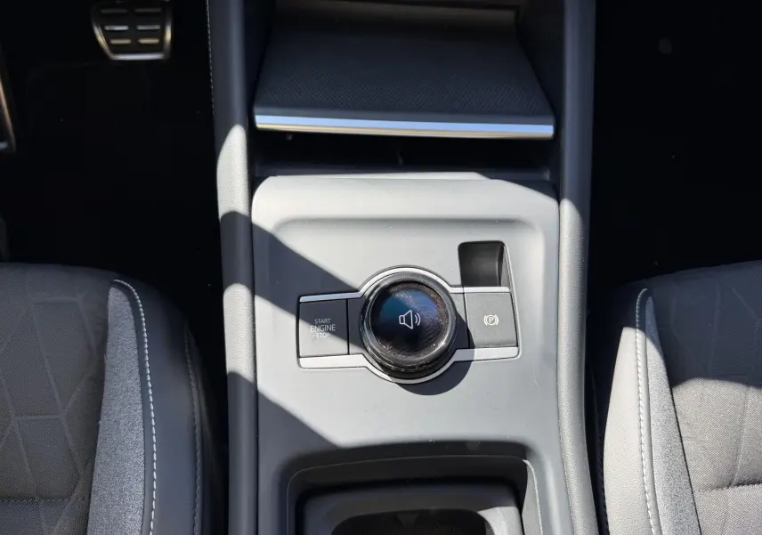 Vue plongeante sur la console centrale grise du Volkswagen Tiguan 2025 avec bouton start/stop et molette de contrôle audio.