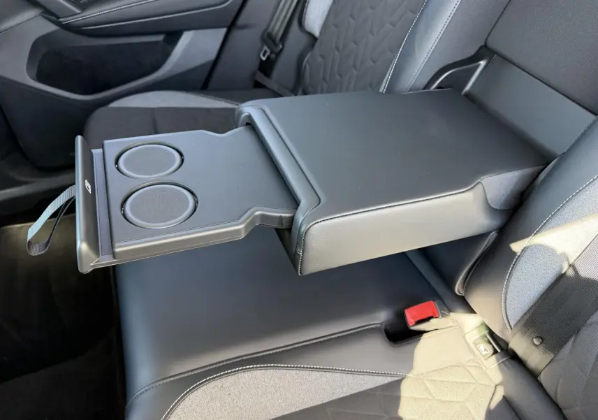 Vue intérieure du siège arrière du Volkswagen Tiguan 2025 avec accoudoir central noir et porte-gobelets déployé.