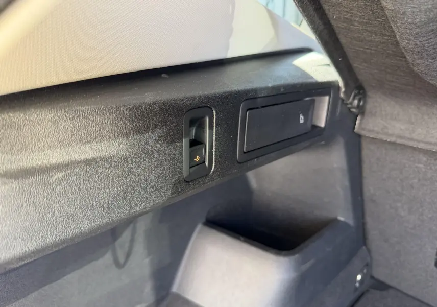 Détail intérieur du coffre du Volkswagen Tiguan 2025, montrant un bouton de rabattement de siège et un compartiment de rangement noir.