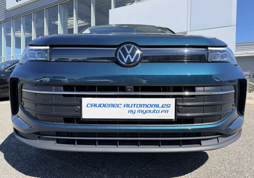 Vue frontale rapprochée du Volkswagen Tiguan bleu 2025 avec calandre noire et logo VW central lumineux.