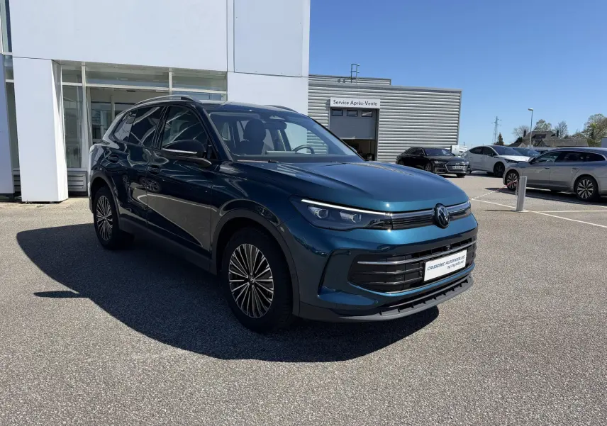 Volkswagen Tiguan bleu en 3/4 avant droit, avec jantes alliage et calandre noire brillante, stationné devant un bâtiment.