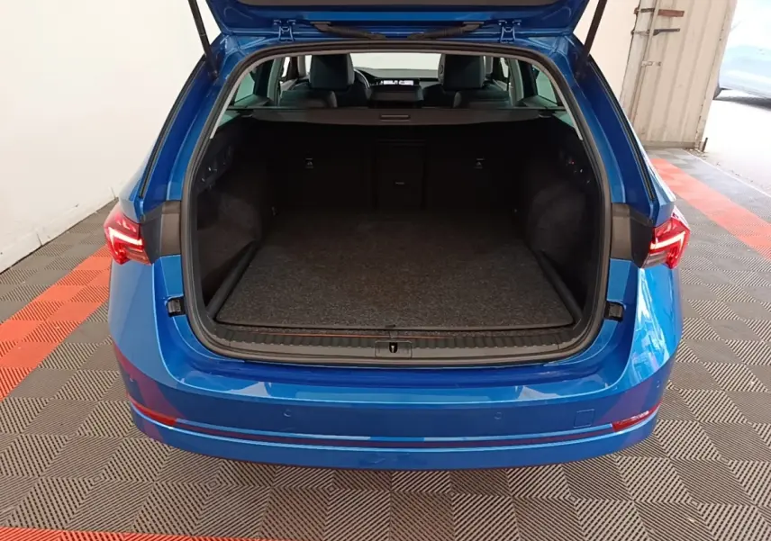 Vue arrière d'un Skoda Octavia bleu 2022 avec coffre ouvert montrant un espace de chargement spacieux et tapis gris.