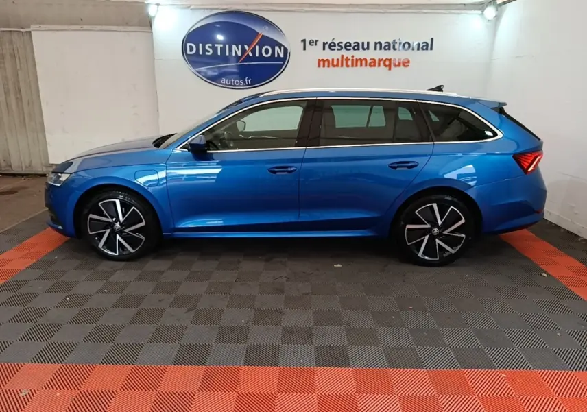 Vue de profil côté gauche d'une Skoda Octavia break bleu 2022 hybride rechargeable, jantes alliage noires et argent.
