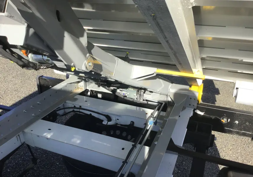 Gros plan sous la benne relevée du Ford Transit Chassis Cabine blanc, montrant le bras polybenne et la structure métallique.