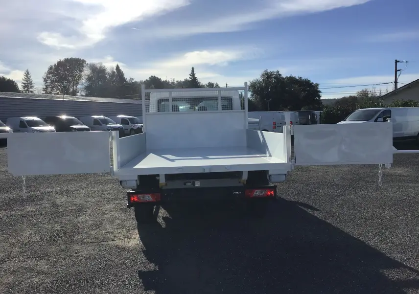 Vue arrière d'un Ford Transit blanc avec benne ouverte et bras polybenne, sur un parking extérieur ensoleillé.