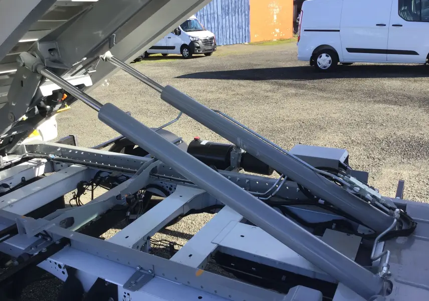 Gros plan sur le bras polybenne relevé du Ford Transit Chassis Cabine blanc, montrant le mécanisme hydraulique et la benne ouverte.