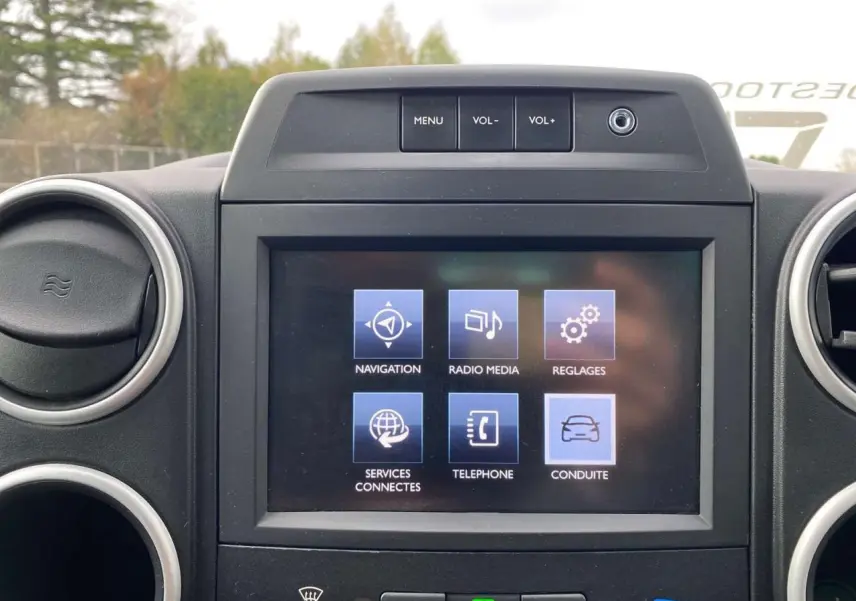 Écran tactile multifonctions allumé au centre du tableau de bord du Peugeot Partner gris, entouré de bouches d'aération rondes.