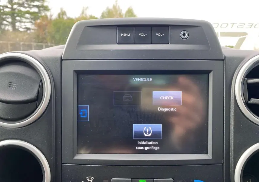 Écran tactile multifonctions allumé au tableau de bord du Peugeot Partner gris, avec commandes de volume visibles.