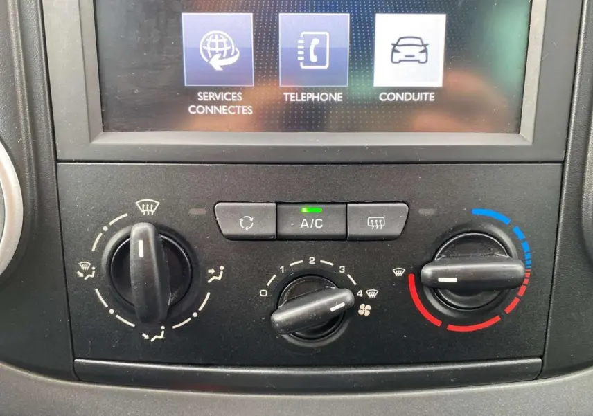 Gros plan sur la console centrale du Peugeot Partner gris, montrant les commandes de climatisation et l'écran tactile multifonctions.
