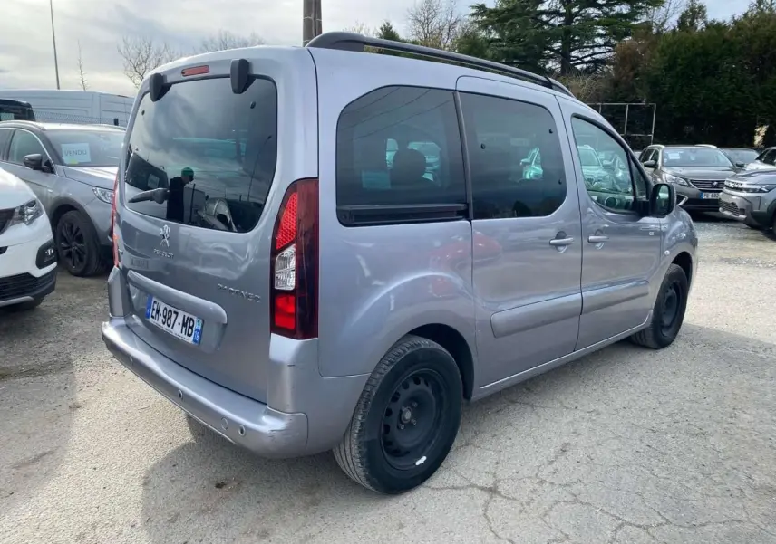 Vue 3/4 arrière droite d'un Peugeot Partner gris Artense avec porte latérale coulissante et roue de secours noire.