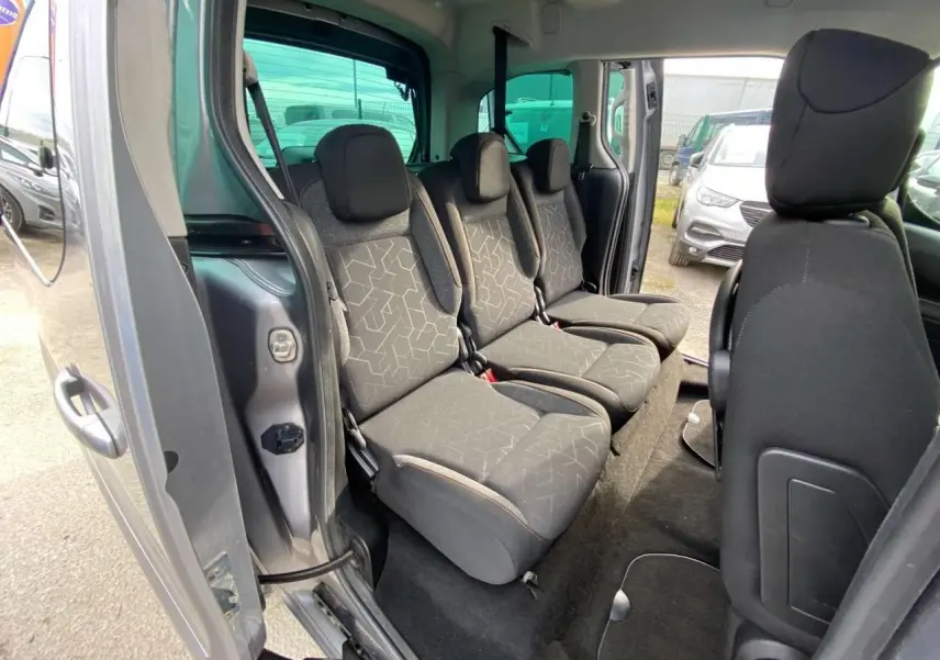 Vue intérieure côté gauche du Peugeot Partner gris Artense, montrant la banquette arrière 2/3-1/3 avec sièges en tissu noir.