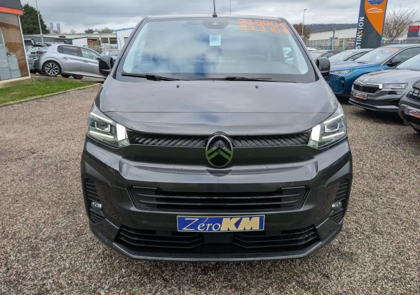 Vue frontale d'un Citroën Jumpy gris avec phares LED allumés et plaque Zéro KM sur un parking.