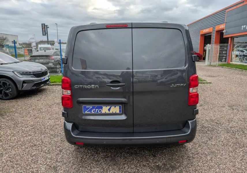 Vue arrière d'un Citroën Jumpy gris foncé avec portes battantes et feux rouges visibles sur un parking.