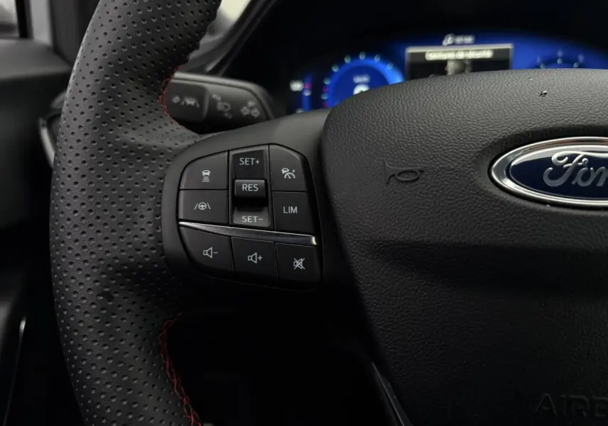 Gros plan sur le volant perforé noir avec surpiqûres rouges du Ford Puma 2023, montrant les commandes multifonctions à gauche.