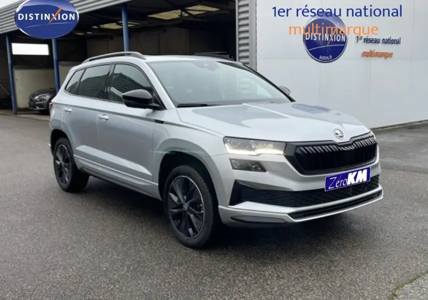 Vue 3/4 avant droite d'un Skoda Karoq gris argent métallisé avec calandre noire et jantes foncées, stationné devant un bâtiment.