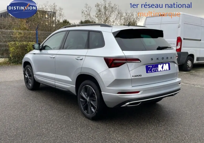 Vue 3/4 arrière droite d'un Skoda Karoq gris argent métallisé avec jantes noires et feux arrière LED distinctifs.