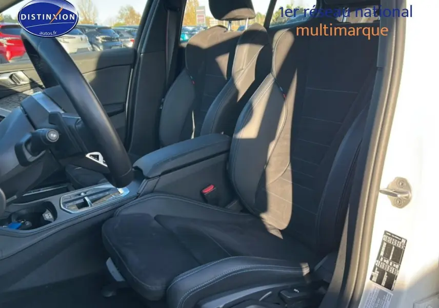 Vue intérieure côté conducteur de la BMW Série 1 blanche, sièges sport en alcantara noir avec coutures bleues.