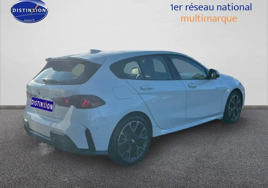 BMW Série 1 blanche vue en 3/4 arrière droit, avec jantes 18 pouces bicolores et becquet arrière sportif.