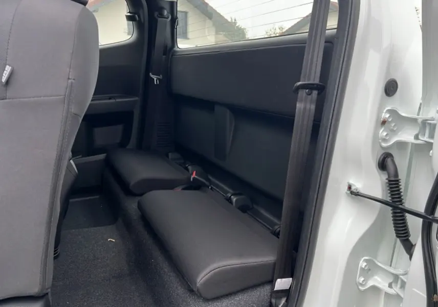 Vue intérieure côté arrière droit du pick-up Isuzu D-MAX Splash white 2026, montrant les sièges strapontins noirs et la portière ouverte.