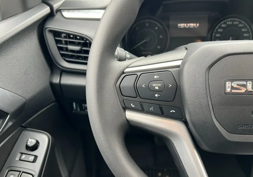 Gros plan sur le volant multifonctions noir de l'Isuzu D-MAX 2026 avec commandes audio et logo central visible.