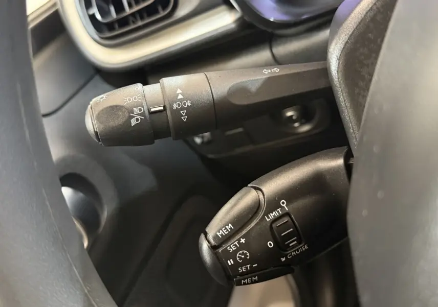 Gros plan sur les commandes au volant noir du Citroën C3 blanc, mettant en valeur les boutons du régulateur de vitesse et des feux.