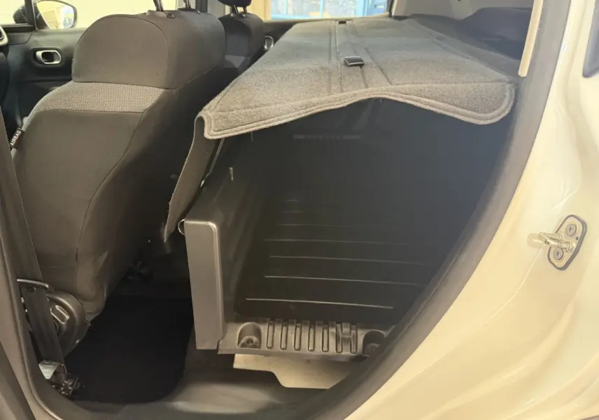 Vue intérieure côté droit du coffre ouvert d'une Citroën C3 blanche avec banquette arrière rabattue et cache-bagages déployé.