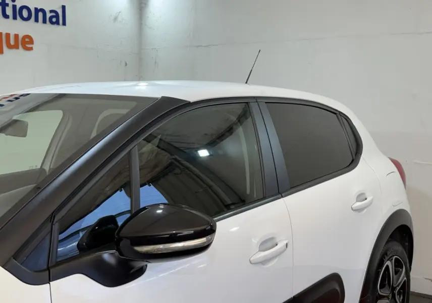 Vue de profil côté gauche d'une Citroën C3 blanche avec rétroviseur noir et vitres teintées dans un garage.