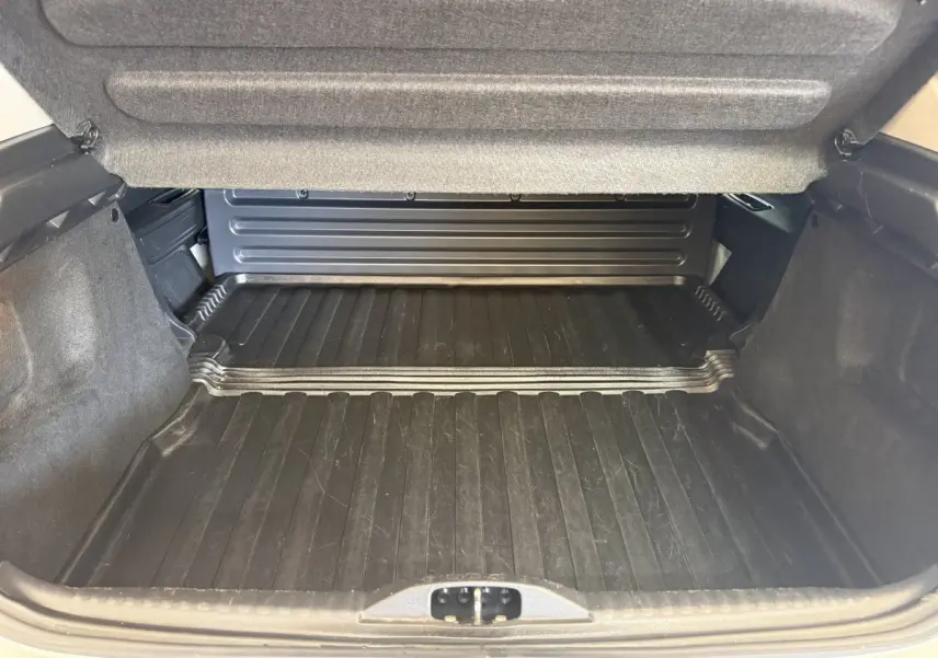 Vue intérieure du coffre ouvert de la Citroën C3 blanche, montrant le tapis de protection noir et les parois rembourrées.