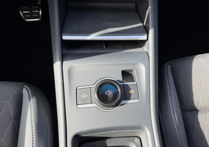 Vue plongeante sur la console centrale grise du Volkswagen Tiguan 2025, avec bouton Start/Stop et commande sonore.